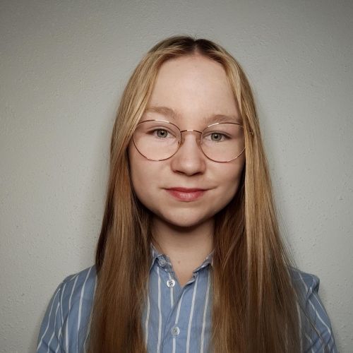 Eine junge Person mit langen, blonden Haaren und einer Brille trägt ein blau-weiß gestreiftes Hemd.